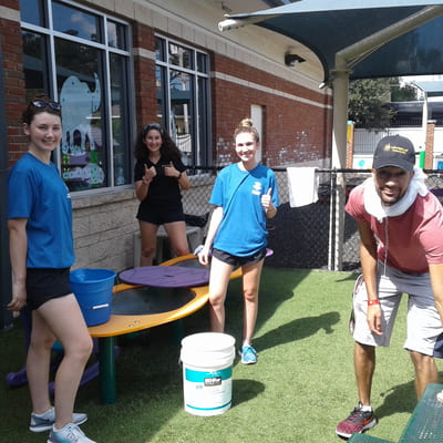 A group of four young Orlando Day Nursery volunteers happily cleaning up the outdoor area of the facility