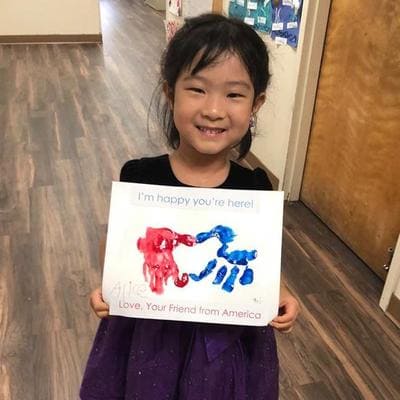 A young little girl holding a white piece of paper with her handprints in red and blue